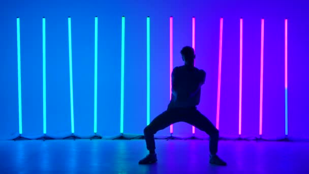 Silhouette of a stylish young man dancing and performing contemporary choreography. Street dance among bright flashing multicolored neon lights. Hip hop technique teaching concept. Slow motion. — Stock Video