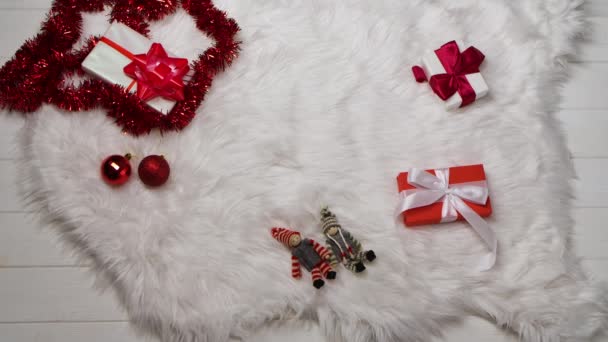Vrouwen handen plaats een geschenkdoos op een witte vacht huid, rond een verspreide rode tinsel en decoraties voor de kerstboom. Wintervakantie Kerstmis en Nieuwjaar. Sluit maar af. Langzame beweging. — Stockvideo