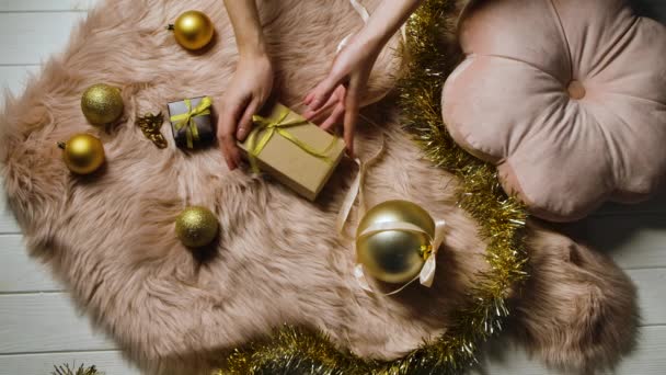 Las manos femeninas ponen la caja de regalo a la piel de la piel. Hojalata y bolas de oro de Navidad se extienden alrededor. Preparándose para felices fiestas de invierno. Humor festivo. Feliz Navidad y año nuevo. De cerca. Movimiento lento. — Vídeo de stock