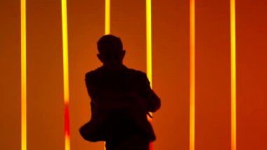 Karanlık bir stüdyoda, parlak kırmızı ve sarı neon ışıkların altında bir break dansçının duygusal performansı. Spor yaşam tarzı konsepti. Erkek silueti yaklaşıyor. Yavaş çekim.