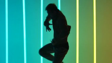 Açık renkli neon ışıkların arka planına karşı karanlık bir stüdyoda profesyonel bir dansçı tarafından gerçekleştirilen break dansın karmaşık unsurları. Erkek silueti yaklaşıyor. Yavaş çekim.