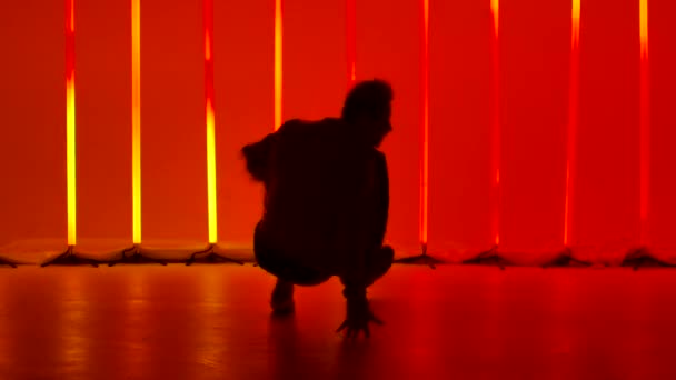 Tarz sahibi erkek break dans dansçısı, karanlık bir stüdyoda kırmızı ve sarı neon tüplerin arka planına karşı bir dönüş yapıyor. Dinamik olarak dans eden bir adamın silueti. Yavaş çekim. — Stok video