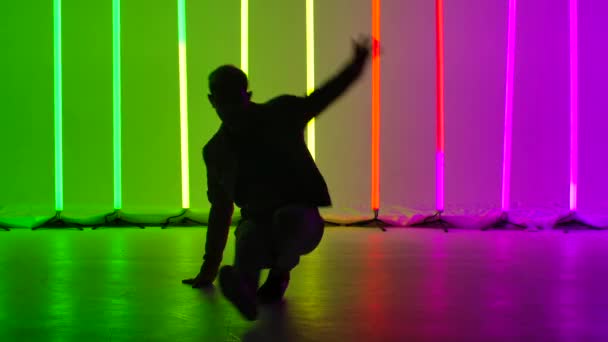 Şık giyinmiş sokak dansçısı erkek dansçı karmaşık dans figürleri ve amuda kalkıyor. Adam becerilerini parlak neon ışıkların arka planında geliştiriyor. Siluet. Kapatın. Yavaş çekim. — Stok video