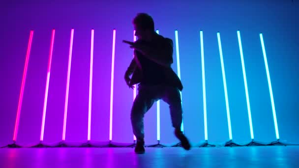 Bottom view of a professional break dancer performing against a backdrop of bright neon lights. Silhouette of stylish street male dancer performing complex dance combinations. Close up. Slow motion. — Stock Video