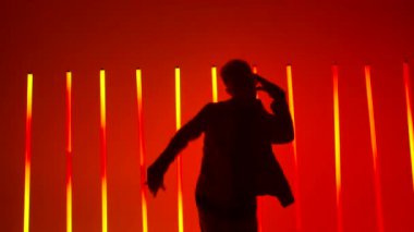 Karanlık bir stüdyoda, parlak kırmızı ve sarı neon ışıkların altında bir break dansçının duygusal performansı. Spor yaşam tarzı konsepti. Kamera hareket halinde. Erkek silueti yaklaşıyor. Yavaş çekim.