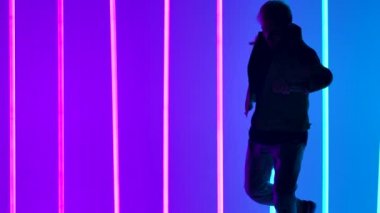 Akrobatik elementlerle sokak dansı. Şık bir adam, parlak neon ışıkların arka planına karşı karmaşık bir takla atar. Siluet. Kapatın. Yavaş çekim.