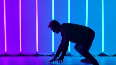 Parlak renkli neon ışıkların arka planına karşı akrobatik dönen elementlerle break dans. Karışık dans numaraları yapan bir adamın silüeti. Kapatın. Yavaş çekim.