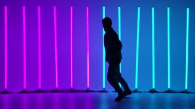 Akrobatik elementlerle sokak dansı. Şık bir adam, parlak neon ışıkların arka planına karşı karmaşık bir takla atar. Siluet. Yavaş çekim.