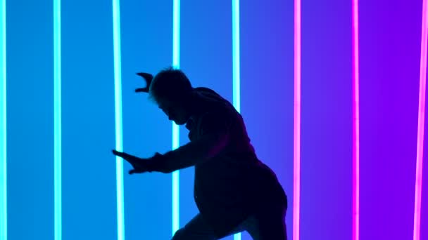 Breakdancing akrobatikus elemek által végzett profi táncos hátterében fényes színes neon fények. Silhouette az ember elvégzi a kézenállás és a forgás. Közelről. Lassú mozgás. — Stock videók