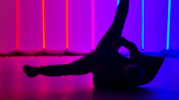 Experienced dancer performs complex break dance elements, spins on the floor and does a headstand. Silhouette of a man against the background of bright multi-colored neon lights. Close up. Slow motion — Stok video