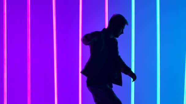 A stylish breakdancing dance show performed by a professional dancer. Silhouette of a man in youth clothes dancing against the background of bright colored neon lights. Close up. Slow motion. — Stock Video