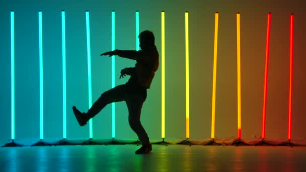 Elementi complessi di break dance eseguiti da un ballerino professionista in uno studio buio su uno sfondo di luminose luci al neon multicolore. Silhouette. Rallentatore. — Video Stock