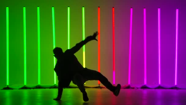 Pouliční mužský tanečník ve stylovém oblečení provádí komplexní taneční breakdance prvky a handstands. Člověk cvičí své schopnosti na pozadí jasných neonových světel. Silueta. Zpomalený pohyb. — Stock video