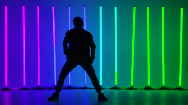 Un breakdancer professionnel effectue des rotations manuelles complexes. Silhouette d'un homme dansant sur fond de néons lumineux dans un studio crépusculaire. Mouvement lent. — Video