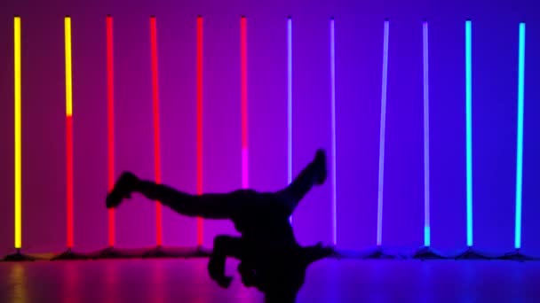 Breakdance akrobatiska element som utförs av en professionell dansare mot bakgrund av ljusa flerfärgade neonljus. Silhuett av en man som utför ett handstativ och rotation. Långsamma rörelser. — Stockvideo