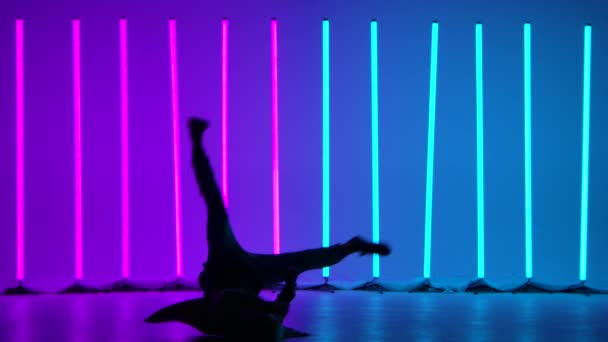 Experienced dancer performs complex break dance elements, rotates on the floor and does a handstand. Silhouette of a man against the background of bright multicolored neon lights. Slow motion. — Stockvideo
