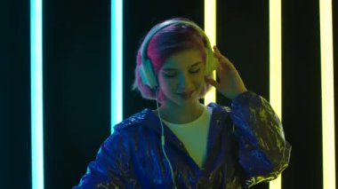 Büyük beyaz kulaklıklı genç bir kadının portresi dans ediyor ve müzikten hoşlanıyor. Kapatın. Yavaş çekim.