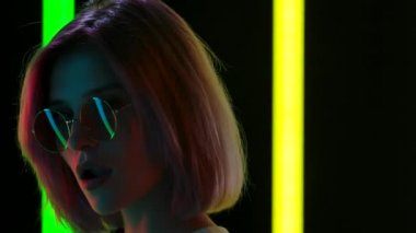 Güneş gözlüklü, sakız çiğneyen ve baloncuk çıkaran genç bir kadının portresi. Kapatın. Yavaş çekim.