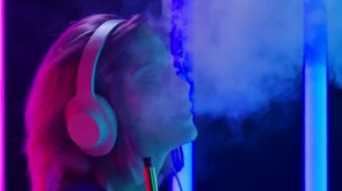 Genç ve şık bir kadının portresi büyük beyaz kulaklıklarla müzik dinliyor, dans ediyor ve zevkle nargile içiyor. Kapatın. Yavaş çekim.