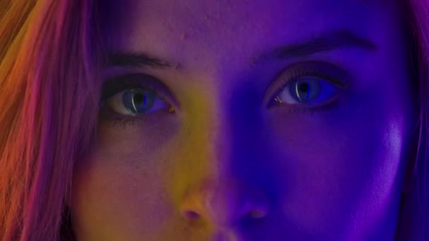 Doğal makyajlı, renkli neon ışıkla aydınlatılmış kadın gözleri, önüne bak. Makro portreyi kapat. Yavaş çekim. — Stok video