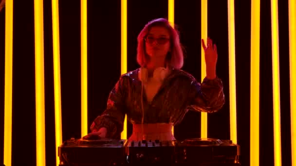 Ritratto di una giovane donna elegante con occhiali da sole e grandi cuffie bianche balla e mescola musica al giradischi DJ. Rallentatore. — Video Stock