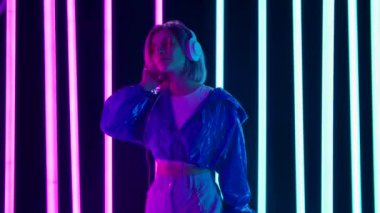 Güneş gözlüklü ve büyük beyaz kulaklıklı genç bir kadının portresi dans ediyor ve yavaş müzikten hoşlanıyor. Yavaş çekim.