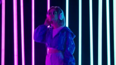 Güneş gözlüklü ve büyük beyaz kulaklıklı genç bir kadının portresi dans ediyor ve yavaş müzikten hoşlanıyor. Yavaş çekim.