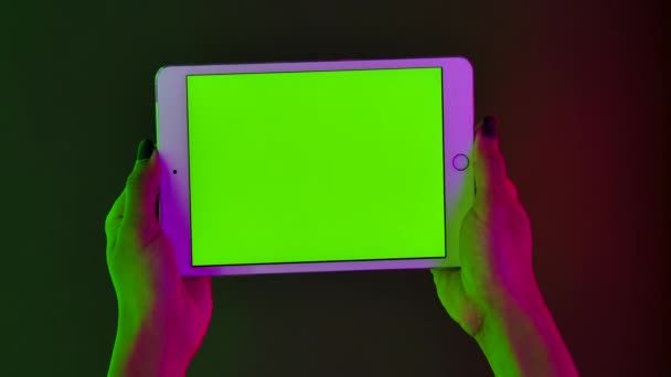 Αφρο-αμερικανίδα γυναίκα κρατά στο χέρι της ένα λευκό δισκίο με ένα πράσινο κλειδί chroma οθόνη. Κοντινό gadget σε οριζόντια θέση με φόντο φωτεινά πολύχρωμα φώτα νέον. Αργή κίνηση. — Αρχείο Βίντεο