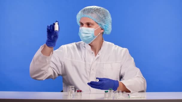 Hälso- och sjukvårdspersonal i skyddsdräkt, mask och handskar undersöker vaccinprover i injektionsflaskor. Covid 19 Coronavirus drog forskning koncept. Blå skärm kromnyckel. Närbild. Långsamma rörelser. — Stockvideo