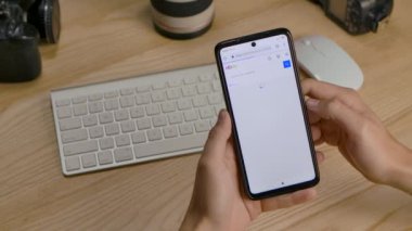 Editör görüntüleri: eBay uygulamasını akıllı telefonda kullanan bir adam, masada oturan fotoğraf ürünlerini araştırıyor. Eller yukarı. Bir bilgisayar masası ve klavyenin arka planındaki telefon ekranını kapat. Yavaş çekim