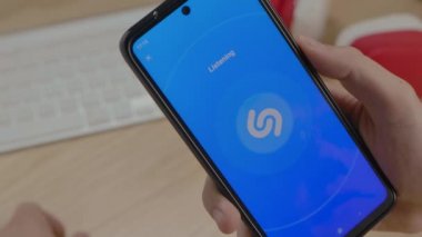 Editör görüntüleri: Erkek eller Shazam uygulamasını akıllı telefonda istediği müziği aramak için kullanıyor. Eller yukarı, kapat. Yavaş çekim.