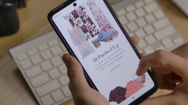 Materiał redakcyjny: Człowiek za pomocą aplikacji Amazon na smartfonie, przeglądając modne ubrania z Vogue siedzi przy biurku. Kupuję prezenty na wakacje online. Ręce na widoku. Zamknij drzwi. Zwolniony ruch. — Wideo stockowe