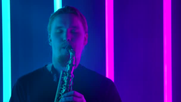 Sólový saxofonista vystupuje v tmavém studiu na pozadí jasných neonových světel. Muž v černém tričku hraje profesionálně na dechový nástroj. Zavřít. Zpomalený pohyb. — Stock video