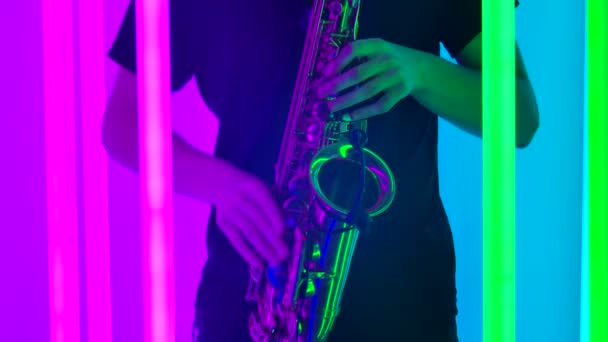 Las manos masculinas están tocando las llaves del saxofón. Un artista saxofonista realiza un concierto en vivo en un estudio oscuro con un telón de fondo de brillantes luces de neón. De cerca. Movimiento lento. — Vídeo de stock