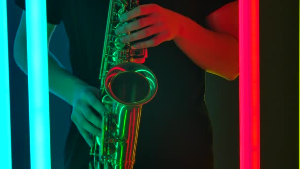 Tangan seorang musisi profesional memainkan saksofon emas. Seorang pria melakukan dengan resital solo di pesta retro dalam gelap terhadap latar belakang lampu neon terang. Tutup. Gerakan lambat. — Stok Video