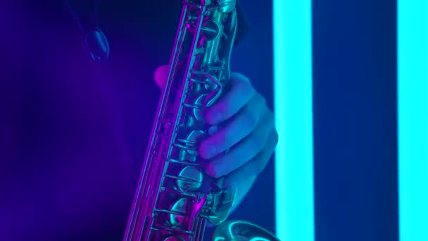 Saxophone doré brillant en gros plan. Images détaillées de mains masculines touchant les touches d'un instrument à vent dans le contexte d'un studio sombre avec des néons brillants. Mouvement lent. — Video