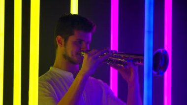 Genç yakışıklı adam trompet çalmaktan hoşlanıyor. Stüdyodaki parlak neon ışıklar arasında müzikal performans. Gece hayatı ve eğlence konsepti. Kapatın. Yavaş çekim.