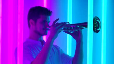 Müzik ve ışık gösterisi. Profesyonel bir trompetçi, parlak neon tüplerle karanlık bir stüdyoda müzik konseri verir. Gece hayatı konsepti. Kapatın. Yavaş çekim.