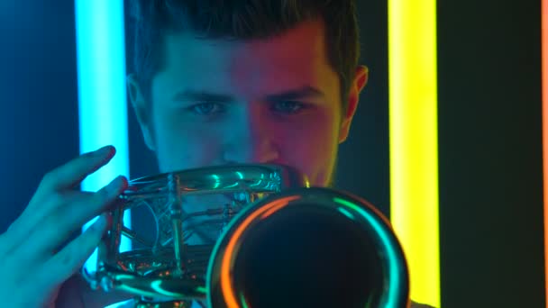Ein Soloauftritt eines professionellen Trompeters in einem dunklen Studio vor dem Hintergrund greller Neonlichter. Zeitlupe. Nahaufnahme. — Stockvideo