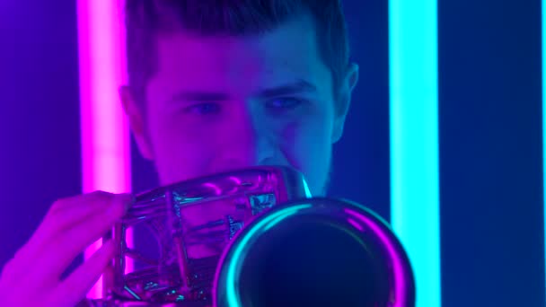 Una actuación en solitario de un trompetista masculino profesional en un estudio oscuro con el telón de fondo de luces de neón de colores brillantes. En cámara lenta. De cerca.. — Vídeo de stock