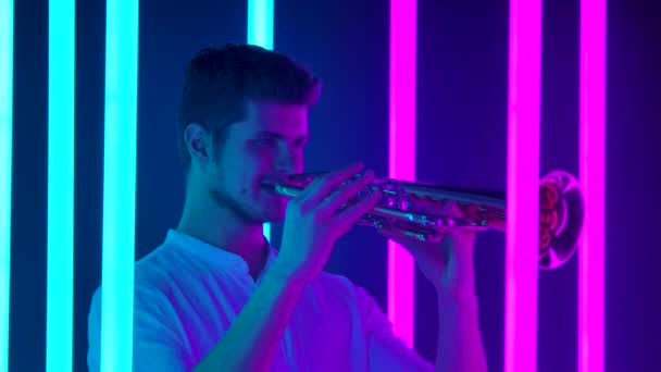 Al joven guapo le gusta tocar la trompeta. Actuación musical entre brillantes luces de neón en el estudio. Vida nocturna y concepto de entretenimiento. De cerca. Movimiento lento. — Vídeos de Stock