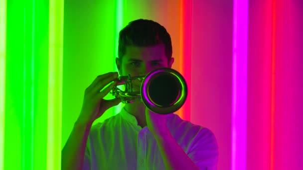 Musical concert of wind instruments. A professional male artist plays classical music on a copper trumpet. Shot in a dark studio with bright neon lights. Close up. Slow motion. — Stock Video