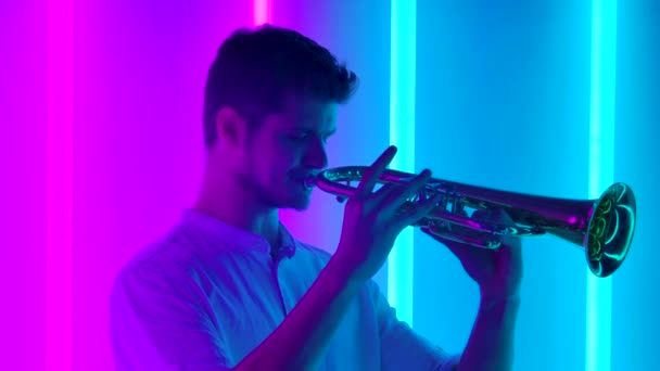 Muestra de música y luces. Un trompetista profesional realiza un concierto de música en un estudio oscuro con tubos de neón multicolores brillantes. Concepto de vida nocturna. De cerca. Movimiento lento. — Vídeo de stock
