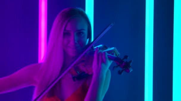 Детальный снимок молодой женщины-музыканта, мастерски играющей на скрипке. Блондинка дотрагивается до струн бантом крупным планом на фоне ярких неоновых огней. Медленное движение. — стоковое видео