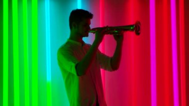 Müzik ve ışık gösterisi. Profesyonel bir trompetçi, parlak neon tüplerle karanlık bir stüdyoda müzik konseri verir. Gece hayatı konsepti. Yavaş çekim.