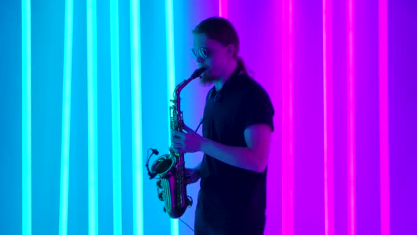 O músico elegante em óculos de sol toca o saxofone. Um homem se apresentando ao vivo em uma festa retro com luzes de néon brilhantes. Movimento lento. Fechar. — Vídeo de Stock