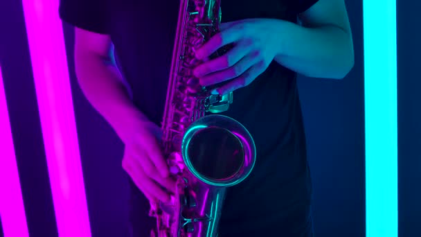 Las manos masculinas están tocando las llaves del saxofón. Un artista saxofonista realiza un concierto en vivo en un estudio oscuro con un telón de fondo de brillantes luces de neón. De cerca. Movimiento lento. — Vídeos de Stock