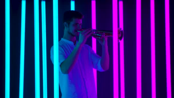 Young handsome man enjoys playing the trumpet. Musical performance among bright neon lights in the studio. Nightlife and entertainment concept. Slow motion. — Stock Video