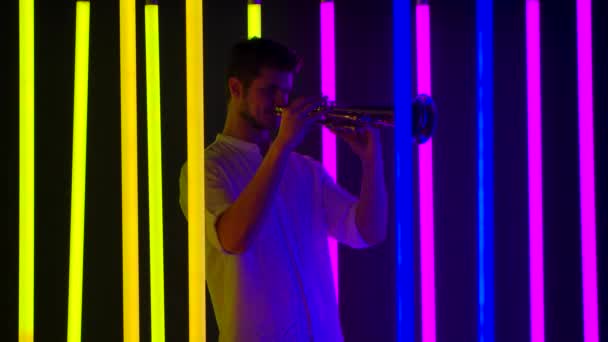 Jonge knappe man speelt graag trompet. Muzikale uitvoering tussen felle neon lichten in de studio. Nachtleven en entertainment concept. Langzame beweging. — Stockvideo