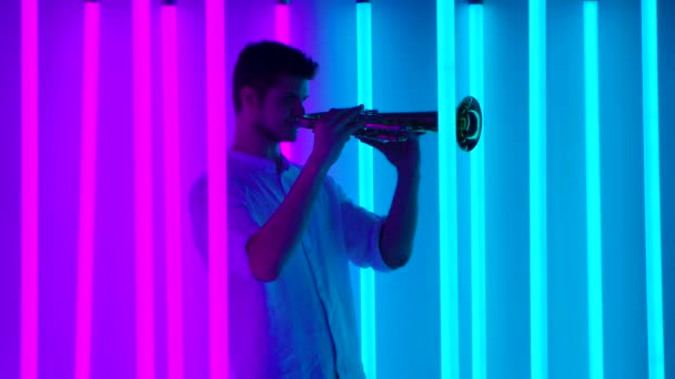 Show von Musik und Licht. Ein professioneller Trompeter gibt in einem dunklen Studio mit hellen, bunten Neonröhren ein Musikkonzert. Nachtleben-Konzept. Zeitlupe. — Stockvideo